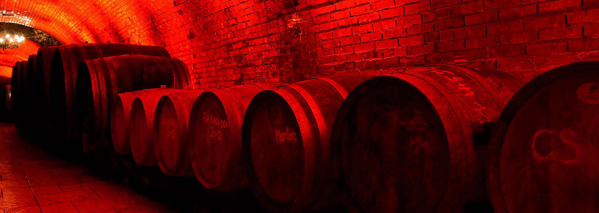 Im Weinkeller stehen große Holzfässer und werden rot beläuchtet.
