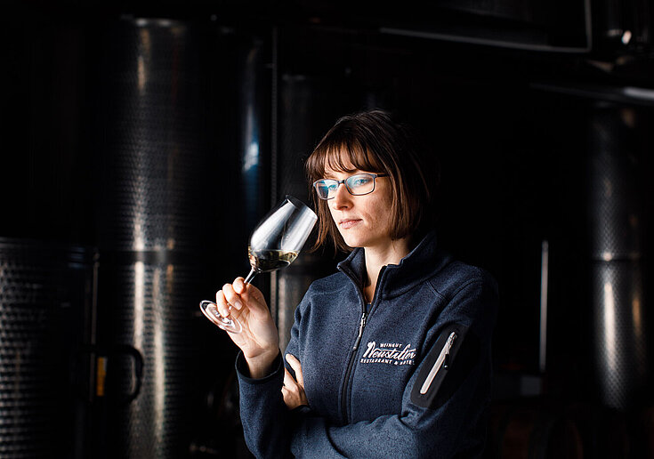 Monika Neustifter steht im dunklen Presshaus vor Stahltanks und riecht an einem Weinglas.