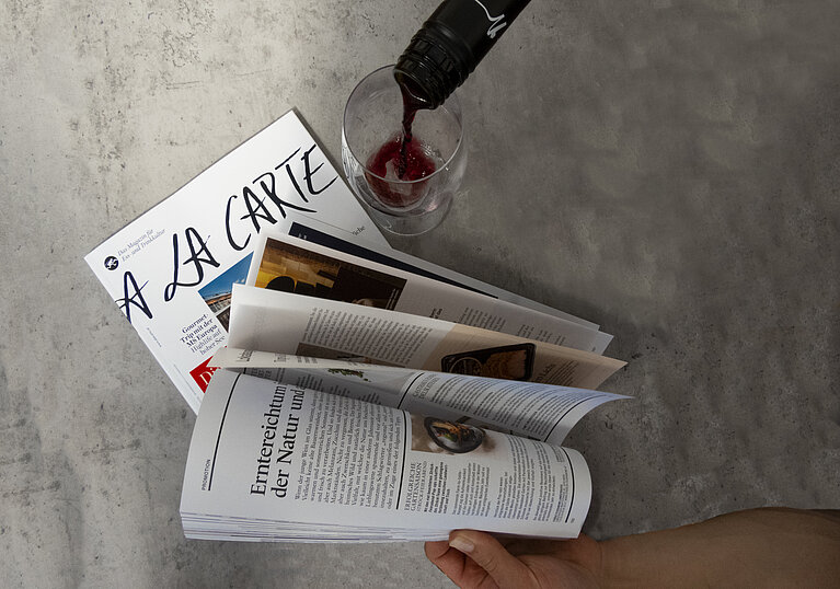 Es wird im A la Carte Magazin herumgeblättert und währenddessen ein Glas Rotwein eingeschenkt.