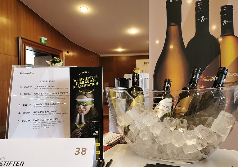 Verkostungsstand DAC Präsentation Der Weingut Neustifter Stand bei der Weinviertel DAC Präsentation. Im Hintergrund befindet sich ein Werberollup. Auf dem Tisch ist ein Weinkühler mit Eiswürfeln und den Weinflaschen, sowie eine Verkostungsliste und Werbematerial der Weinviertel DAC Präsentation.