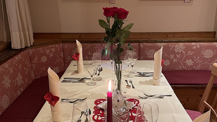 Der Tisch wurde romantisch gedeckt. In der Mitte steht eine Vase mit einer Rose. In den weißen Mundservietten wurden rote Servietten eingearbeitet.