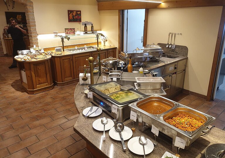 Neujahresbrunch Buffetraum Im Buffetraum steht ein großes Buffet mit Chevingtische in dem warme Hauptspeisen zur freien Entnahme sind. Ganz hinten vom Buffet sind in der Kühlvitrine die Vorspeisen.