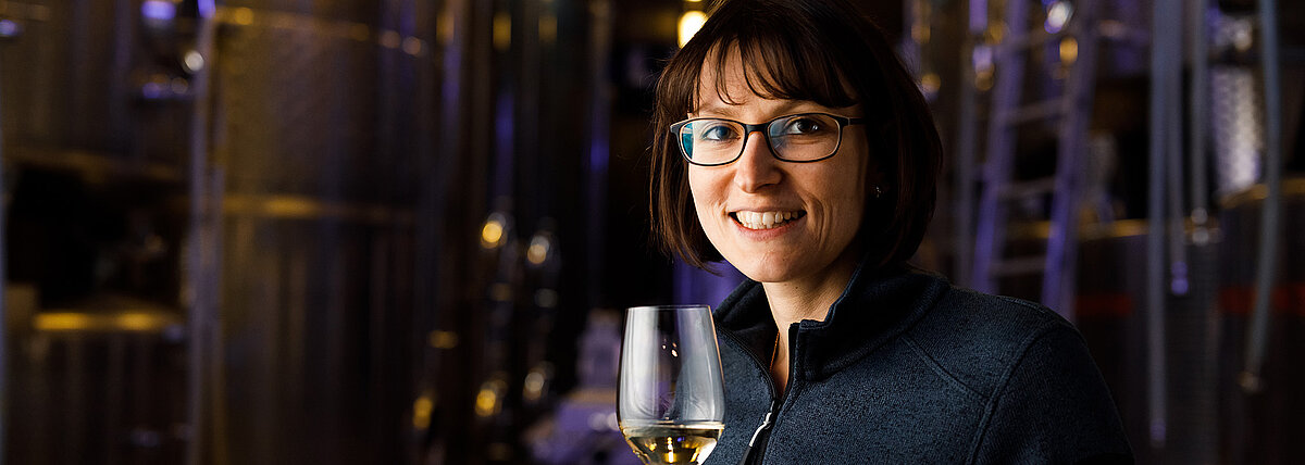 Monika Neustifter steht vor den Stahltanks im Wein.Gut und hält ein Glas Wein in der Hand.