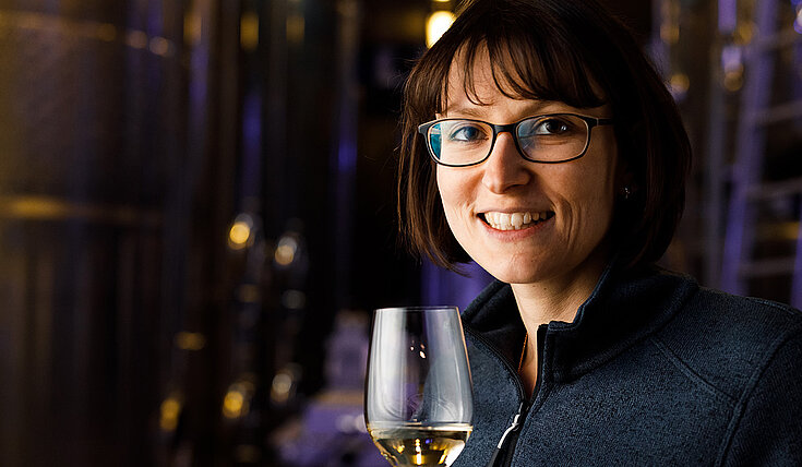 Monika Neustifter steht vor den Stahltanks im Wein.Gut und hält ein Glas Wein in der Hand.