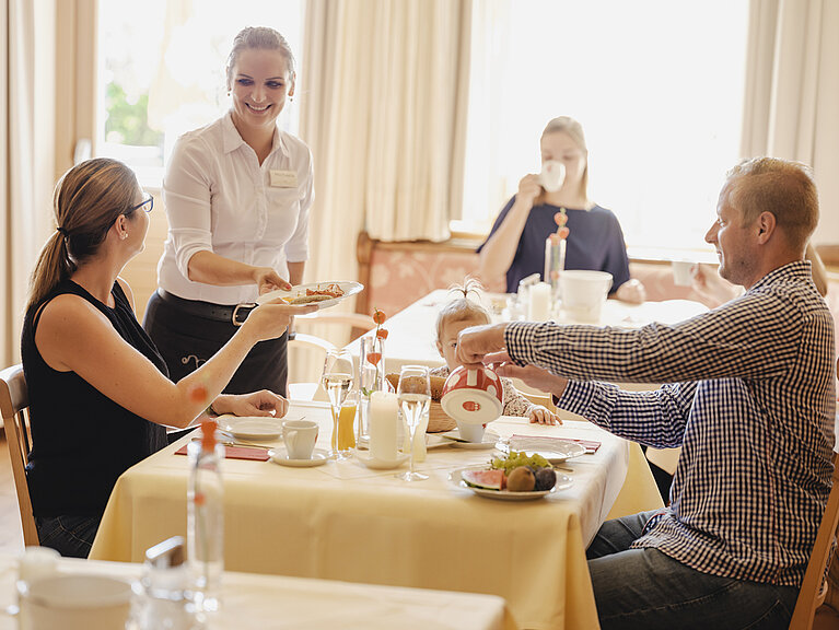 Frühstücksgäste vom Wein.Hotel Neustifter Ein Pärchen sitzt beim Frühstückstisch und eine Kellnerin ist gerade dabei Teller abzuserviren.