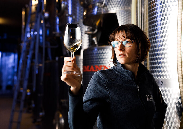 Monika Neustifter hält ein Weißweinglas in die Höhe und steht vor einem Stahltank.