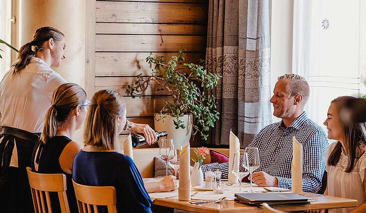 Eine Servicemitarbeiterin schenk Wein bei einem Tisch ein in der Gaststube vom Wein.Restaurant Neustifter.