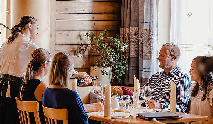 Eine Servicemitarbeiterin schenk Wein bei einem Tisch ein in der Gaststube vom Wein.Restaurant Neustifter.