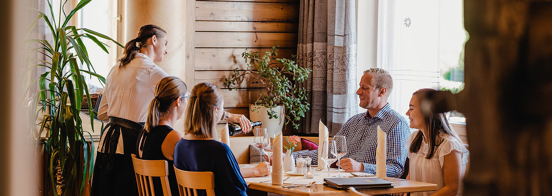 Eine Servicemitarbeiterin schenk Wein bei einem Tisch ein in der Gaststube vom Wein.Restaurant Neustifter.