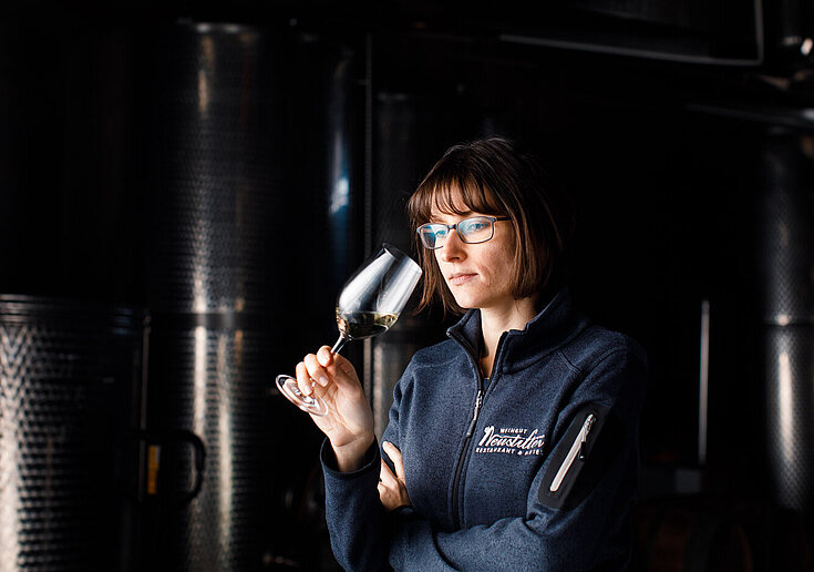 Monika Neustifter steht im dunklen Presshaus vor Stahltanks und riecht an einem Weinglas.