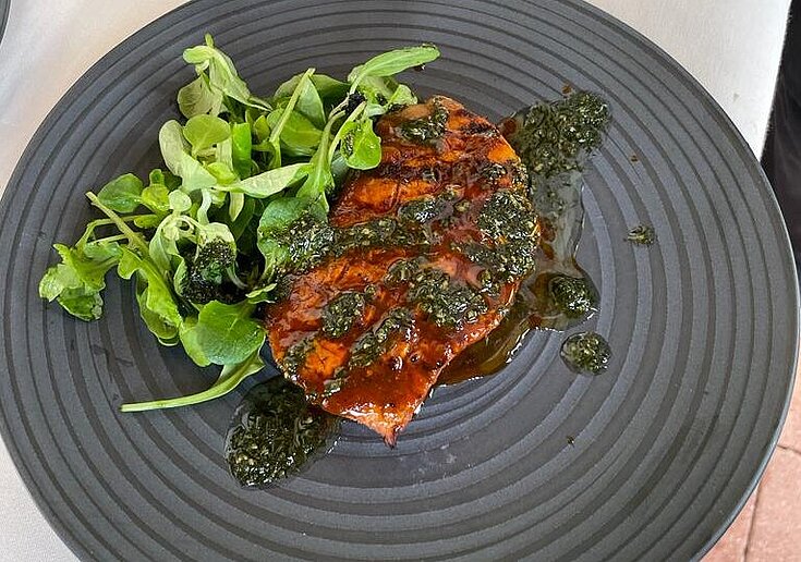 Gegrilltes Steak mit Basilikumpesto und Vogerlsalat liegen auf einem schwarzen Teller.