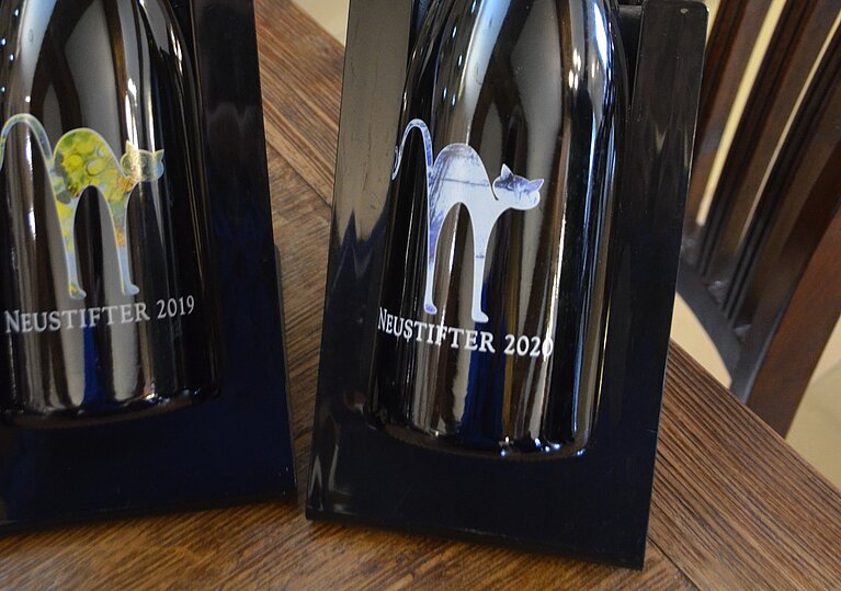 Neustifter Grüner Veltliner Stockkultur 2020 Die Neustifter Grüner Veltliner Stockkultur Flasche liegt in einem schwarzen Kühler auf einem Tisch.
