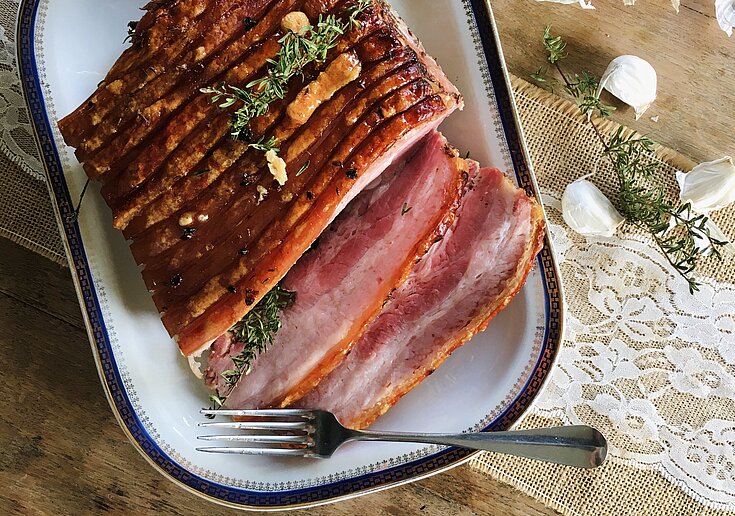 Auf dem rustikalen Tisch steht ein großes Servierteller mit Kümmelbraten, welcher zum Teil schon geschnitten wurde.