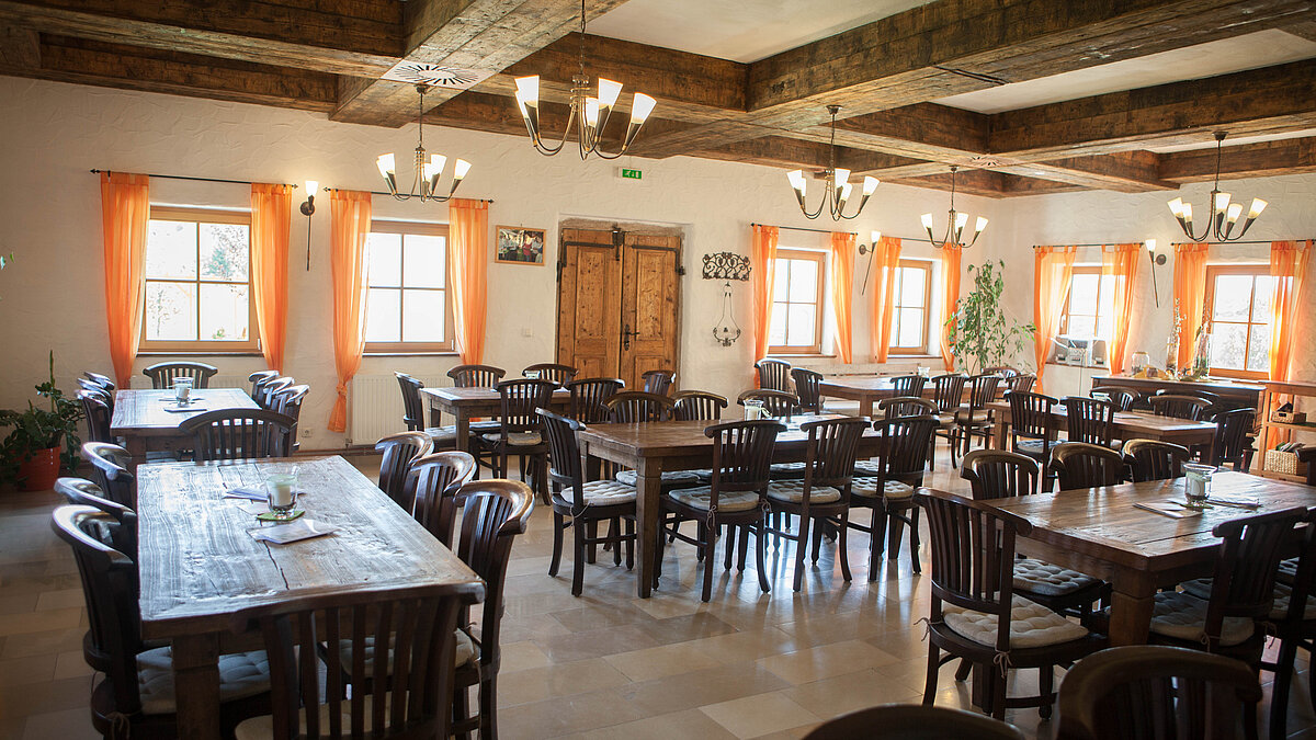 Man sieht den großen Gastraum der Wein.Küche mit orangen Vorhängen großen, massiven Tischen.