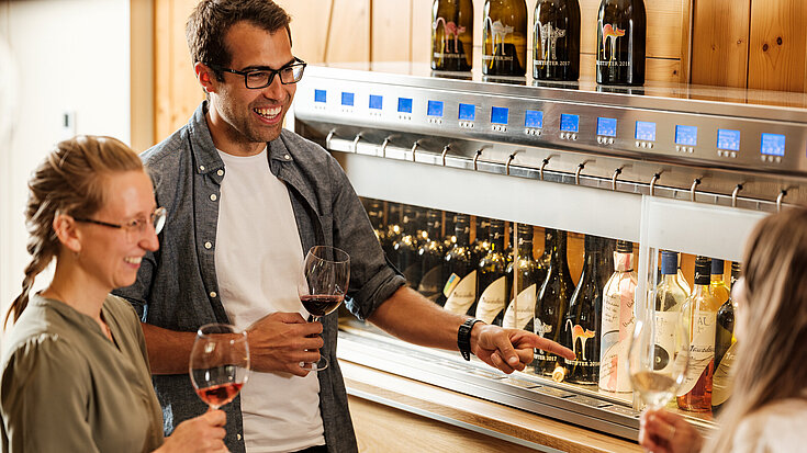 Two people stand in front of the wine vending machine and taste the wine.