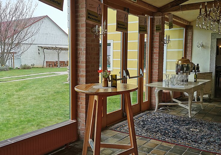 Uprostřed degustační místnosti ve vinařství Wein.Gut Neustifter stojí dřevěný stůl. Velkými okny je výhled ven.