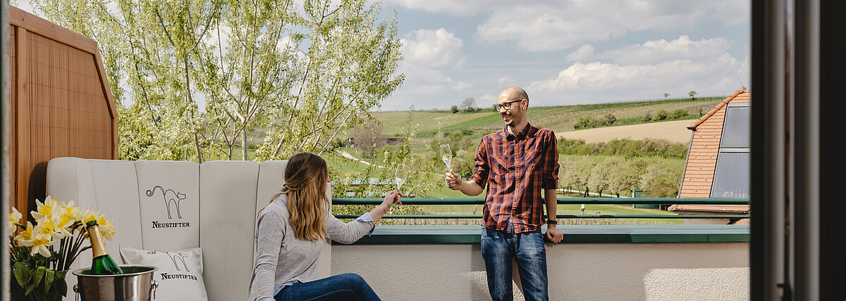 Ein Pärchen steht auf der großen Terrasse eines Exklusiv Zimmers und trinkt ein Glas Sekt.