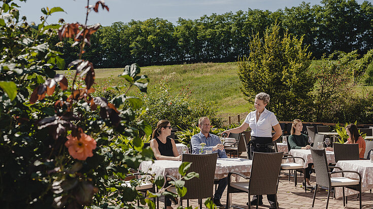 Eine Servicemitarbeiterin bedient Gäste auf der Terrasse vom Wein.Restaurant Neustifter.