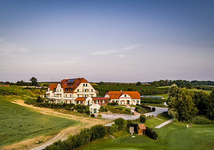 Eine Drohnenaufnahme zeigt im Hintergrund das Wein.Hotel Neustifter. Im Vordergrund steht der nebenanliegenden Golfplatz.