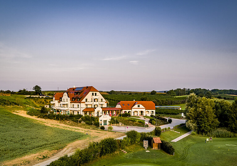 Eine Drohnenaufnahme zeigt im Hintergrund das Wein.Hotel Neustifter. Im Vordergrund steht der nebenanliegenden Golfplatz.