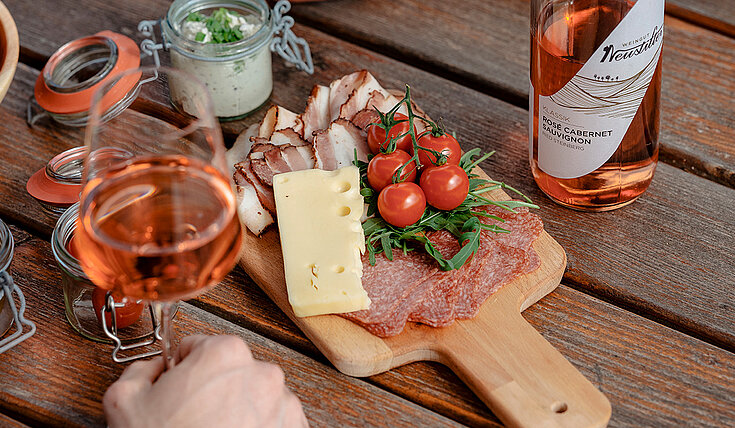 Ein Pärchen sitzt bei Tisch und isst eine Jausenplatte mit Weinviertler Späzialitäten und trinkt dazu ein Glas Neustifter Rosé.