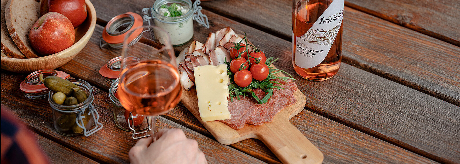 Ein Pärchen sitzt bei Tisch und isst eine Jausenplatte mit Weinviertler Späzialitäten und trinkt dazu ein Glas Neustifter Rosé.