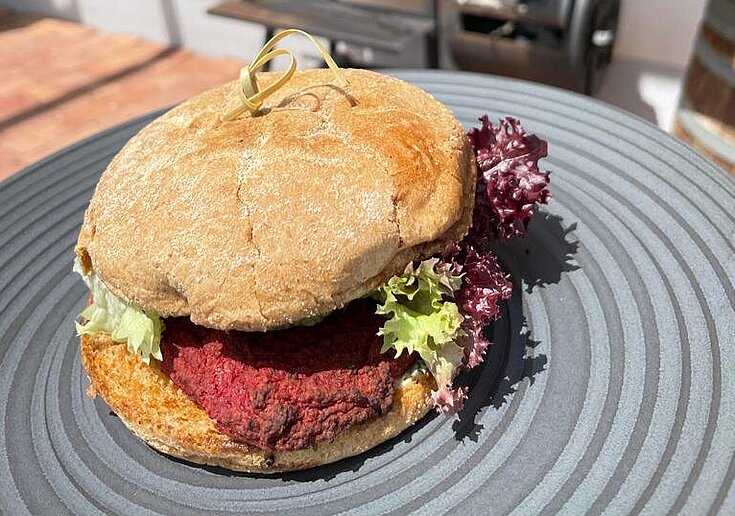 Ein Burger mit selbstgemachtem Patty liegt auf einem schwarzen Teller.
