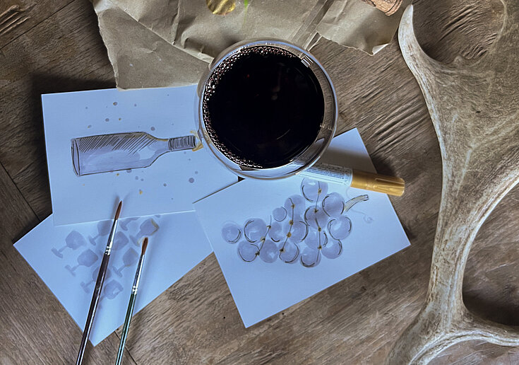 Ein Glas mit Rotwein gefüllt, rundherum liegen selbst gestaltete Weihnachtskarten.