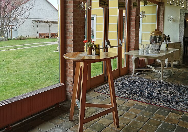 Ein Holzstehtisch steht mitten im Verkostungsraum im Wein.Gut Neustifter. Durch die großen Fenster kann man nach außen sehen.