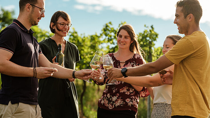 Monika Neustifter macht eine Weinverkostung im Weingarten mit vier jungen Leuten.