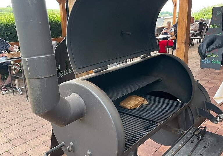 In einem Smoker wird ein Steak gegrillt. Der Smoker steht auf der Terrasse vom Wein.Restaurant Neustifter.