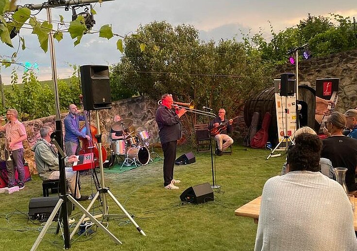 Es dämmert und die Jazzband spielt im Gastgarten der TOP Heuriger Wein.Küche Musik. Gäste sitzen und lauschen den Klängen.